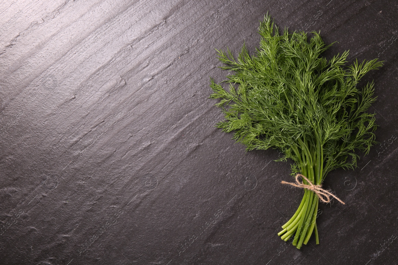 Photo of Bunch of fresh dill on dark textured table, top view. Space for text