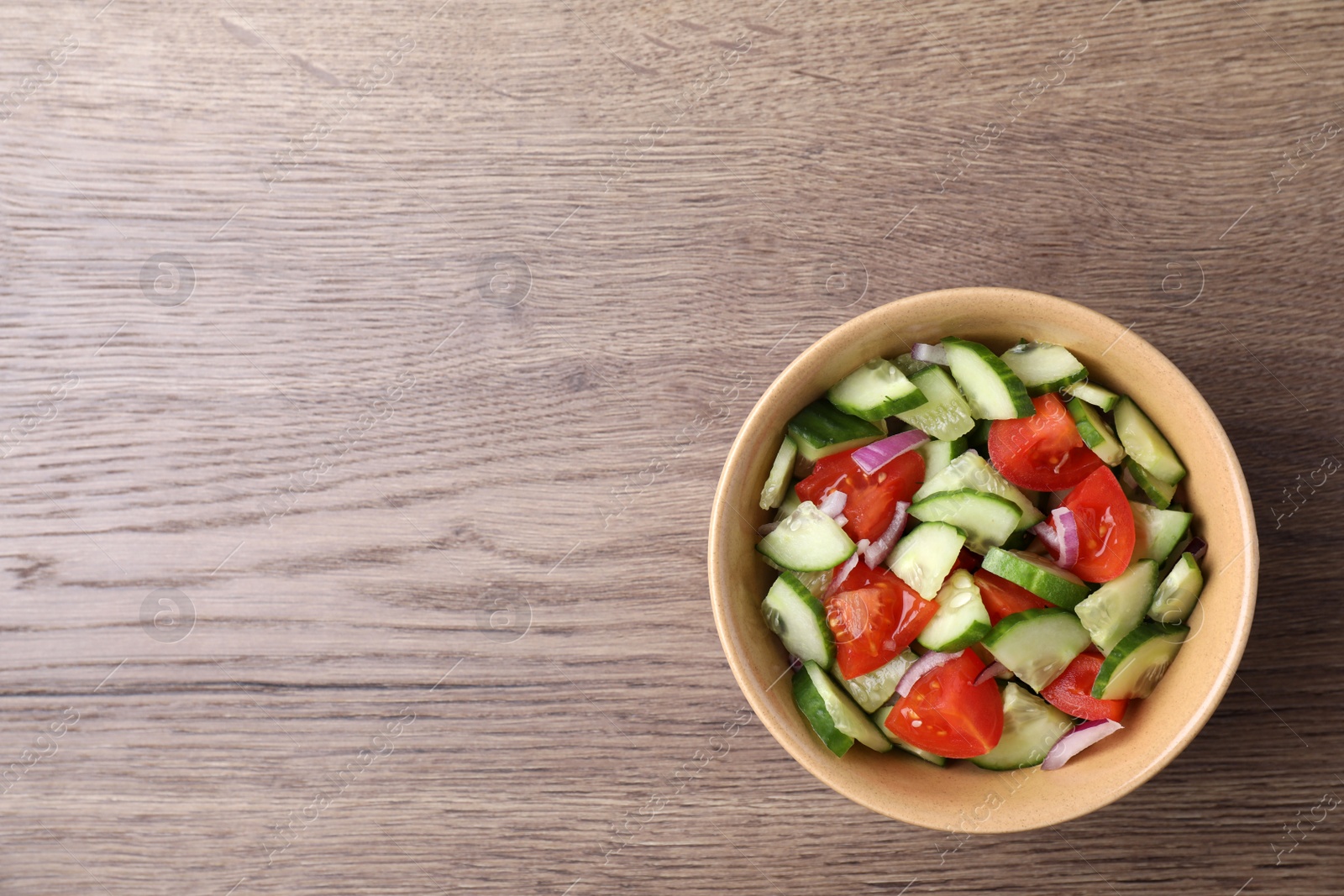 Photo of Bowl of vegetarian salad with cucumber, tomato and onion on wooden background, top view. Space for text