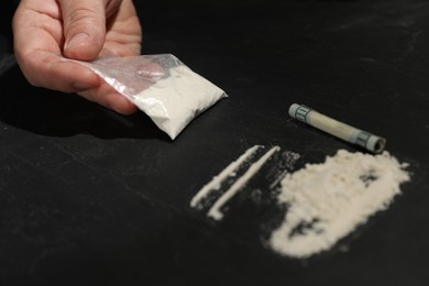 Photo of Drug addiction. Man with cocaine and rolled dollar banknote at dark textured table, closeup