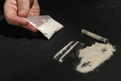 Drug addiction. Man with cocaine and rolled dollar banknote at dark textured table, closeup