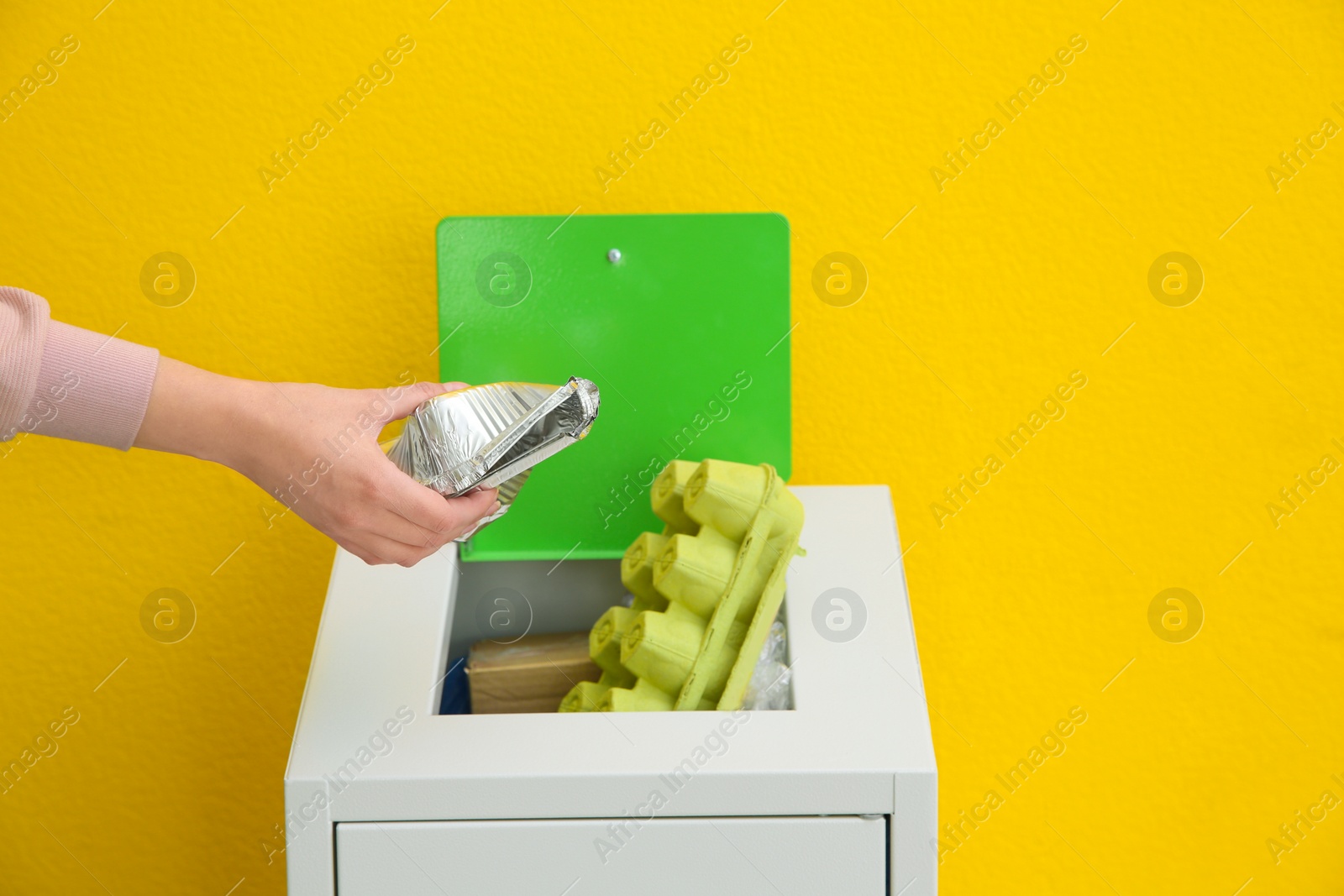 Photo of Woman putting used foil container into trash bin on color background, closeup. Recycling concept