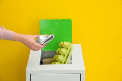 Photo of Woman putting used foil container into trash bin on color background, closeup. Recycling concept