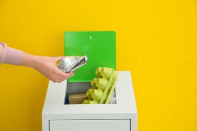 Woman putting used foil container into trash bin on color background, closeup. Recycling concept