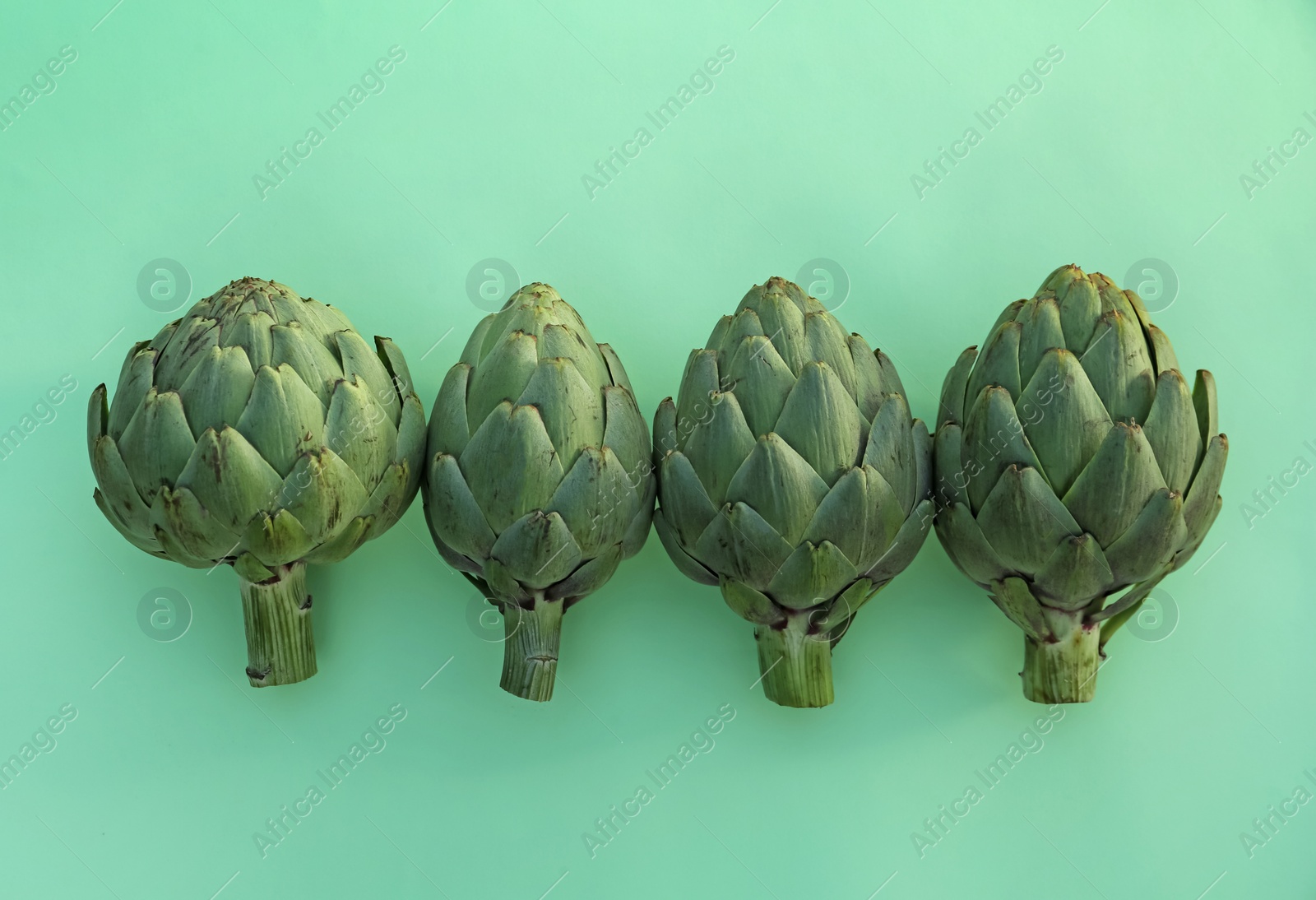 Photo of Whole fresh raw artichokes on green background, flat lay