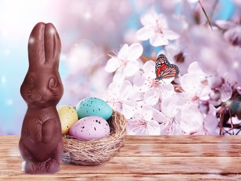 Sweet chocolate bunny and colorful eggs on wooden table outdoors, space for text. Easter celebration