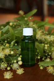Photo of Bottle of essential oil and linden blossoms on wooden table
