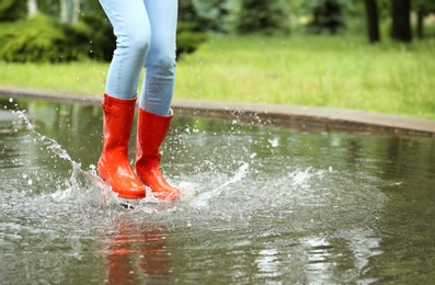 Photo of Woman with red rubber boots jumping in puddle, closeup. Rainy weather