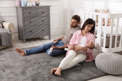 Photo of Tired young parents with their baby sleeping on floor in children's room