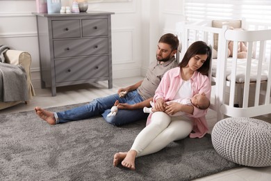 Tired young parents with their baby sleeping on floor in children's room