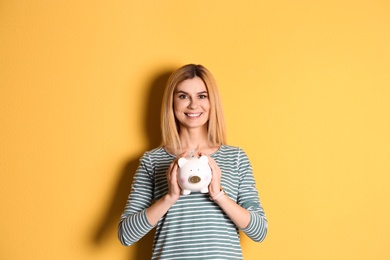 Woman with piggy bank on color background