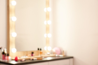 Blurred view of table with makeup products and mirror near white wall, closeup. Dressing room