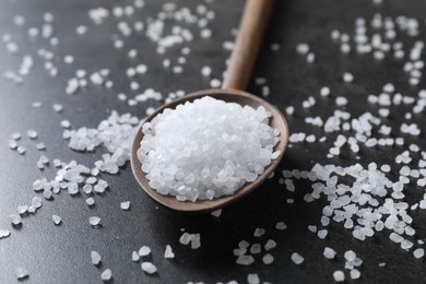 Photo of Natural salt and wooden spoon on black table, closeup