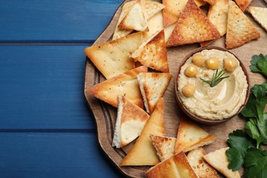 Delicious pita chips with hummus on blue wooden table, top view
