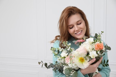 Beautiful woman with bouquet of flowers near white wall indoors. Space for text