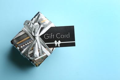 Photo of Gift card and present on light blue background, top view. Space for text