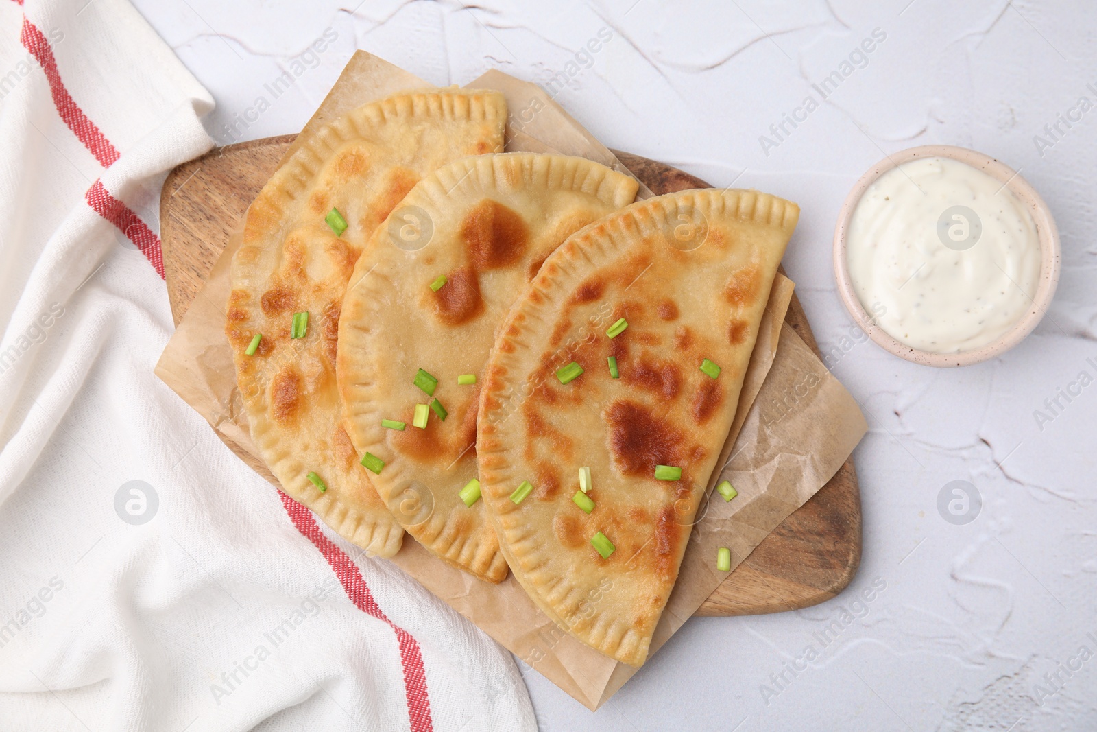 Photo of Delicious fried chebureki with cheese, green onion and sauce on white textured table, flat lay