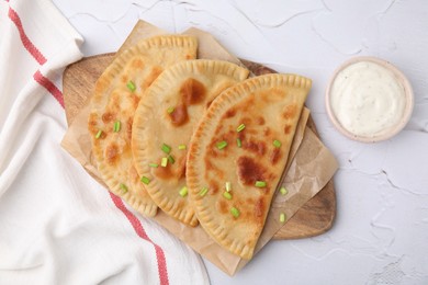 Photo of Delicious fried chebureki with cheese, green onion and sauce on white textured table, flat lay