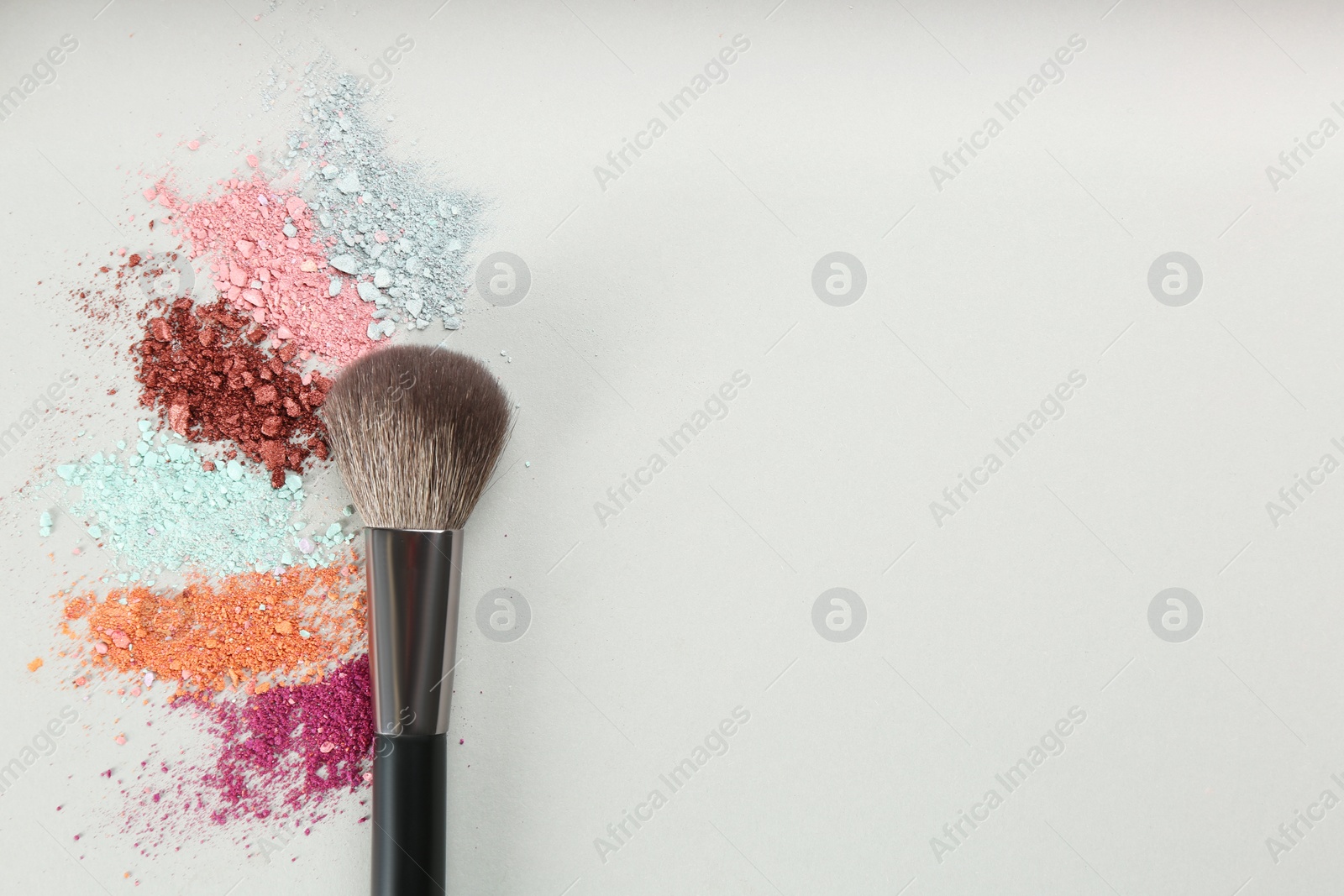 Photo of Makeup brush and scattered eye shadows on light grey background, flat lay. Space for text