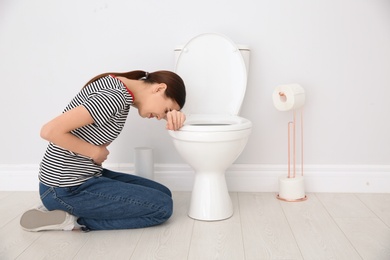 Photo of Young woman suffering from nausea at toilet bowl indoors. Space for text