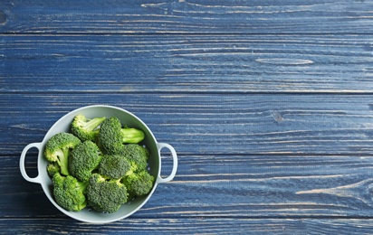 Photo of Colander of fresh broccoli on blue wooden table, top view with space for text