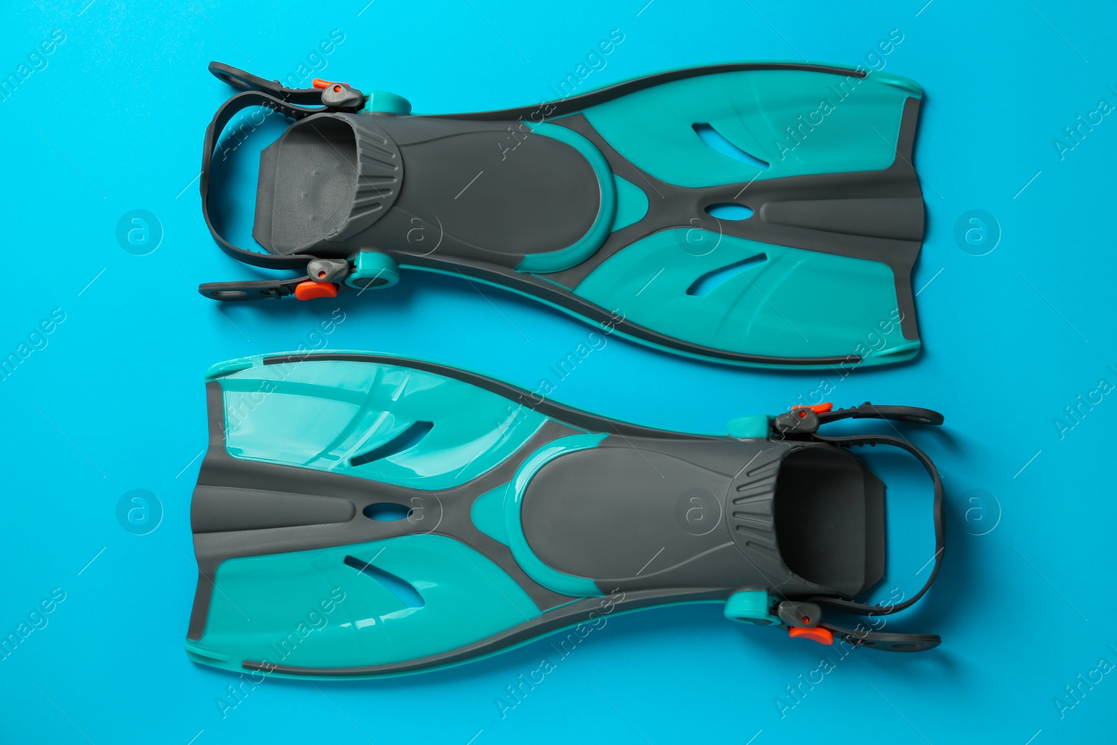 Photo of Pair of turquoise flippers on light blue background, flat lay