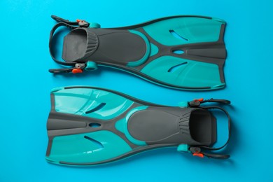 Pair of turquoise flippers on light blue background, flat lay