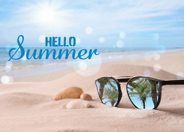 Image of Hello Summer. Sunglasses on sandy beach with seashells near sea