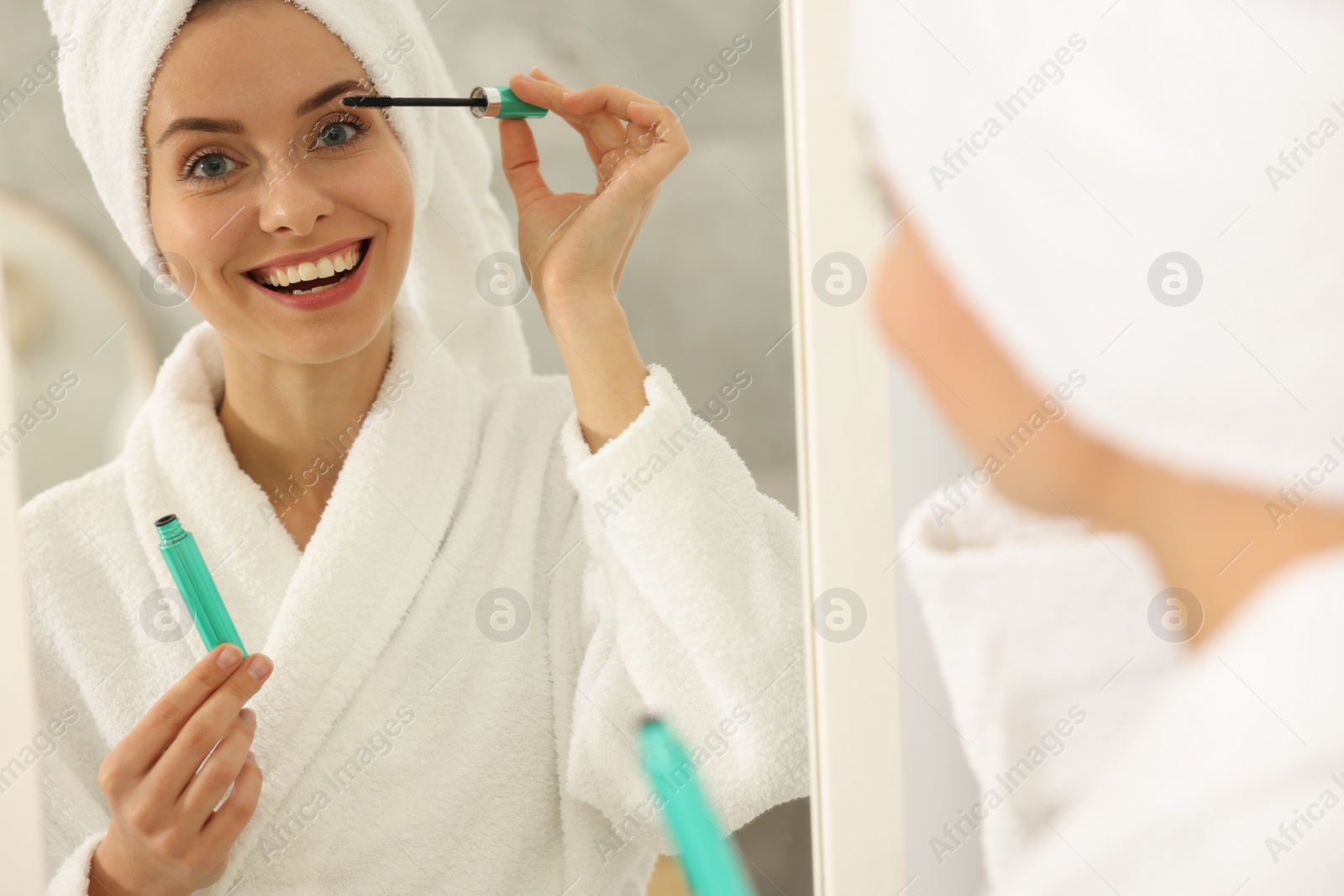 Photo of Beautiful woman applying mascara near mirror in bathroom