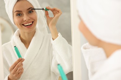 Beautiful woman applying mascara near mirror in bathroom