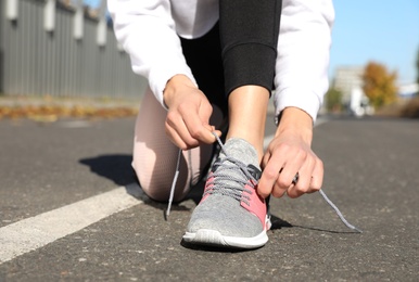 Image of Sporty woman tying shoelaces outdoors on sunny morning, closeup