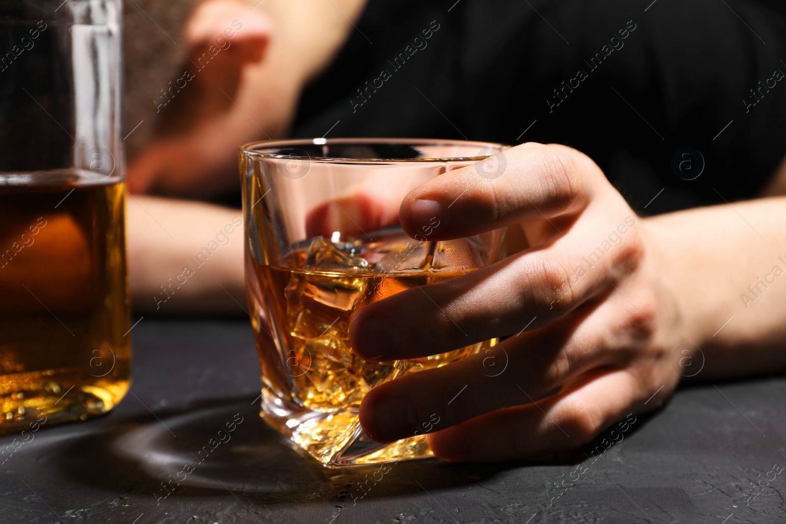 Photo of Alcohol addiction. Man with glass of whiskey at dark textured table, selective focus