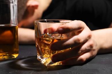 Photo of Alcohol addiction. Man with glass of whiskey at dark textured table, selective focus
