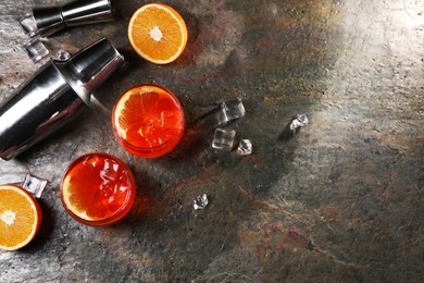 Photo of Aperol spritz cocktail, ice cubes and orange slices in glasses and shaker on grey textured table, flat lay. Space for text