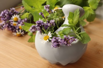 Photo of Mortar with fresh lavender, chamomile flowers, herbs and pestle on wooden table