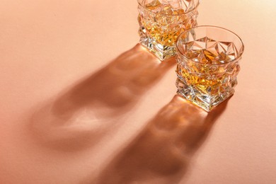 Photo of Whiskey with ice cubes in glasses on coral table, space for text