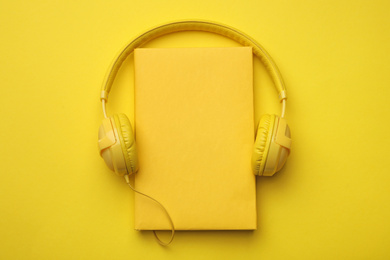 Photo of Book and modern headphones on yellow background, top view