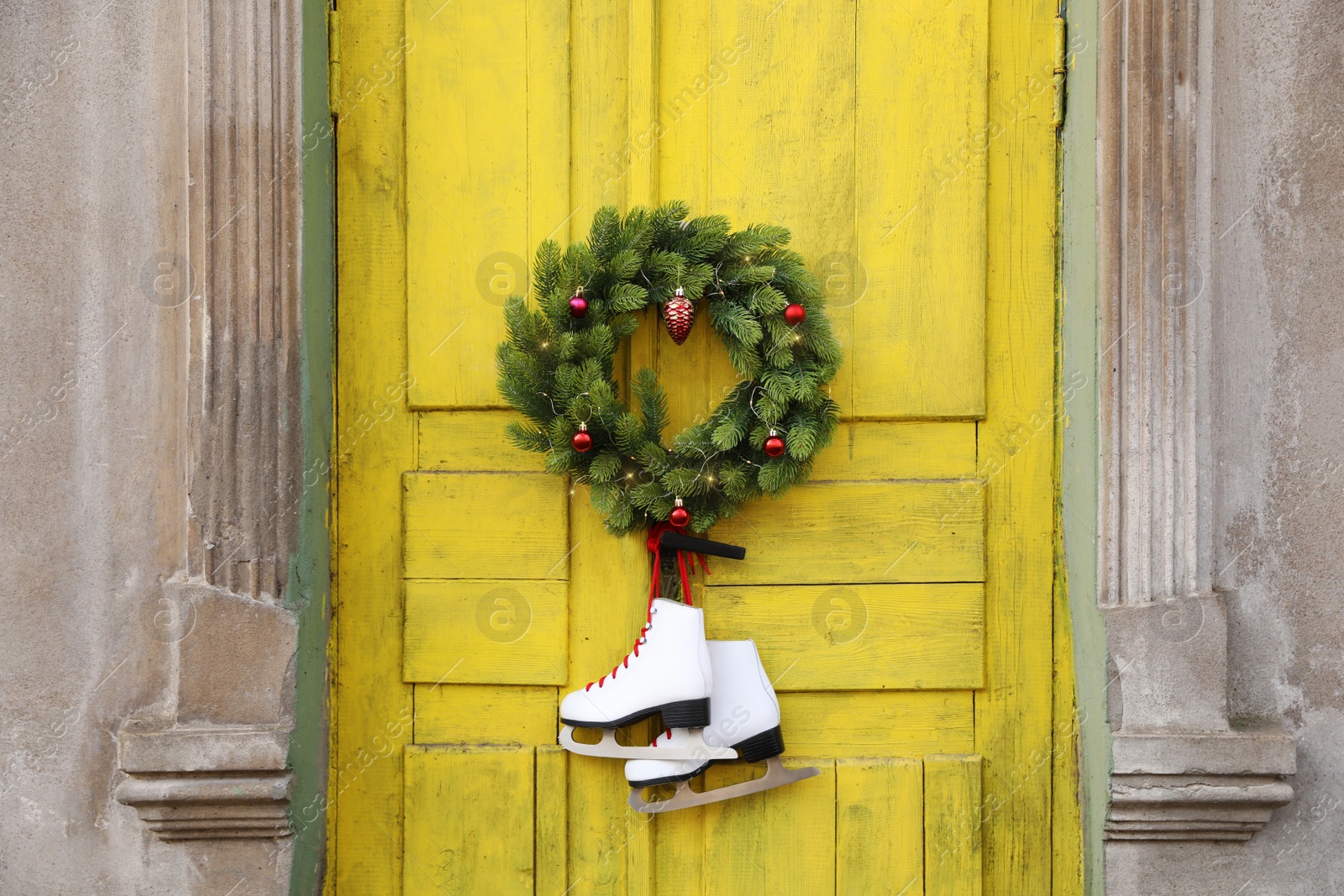 Photo of Pair of ice skates and Christmas wreath hanging on old yellow door