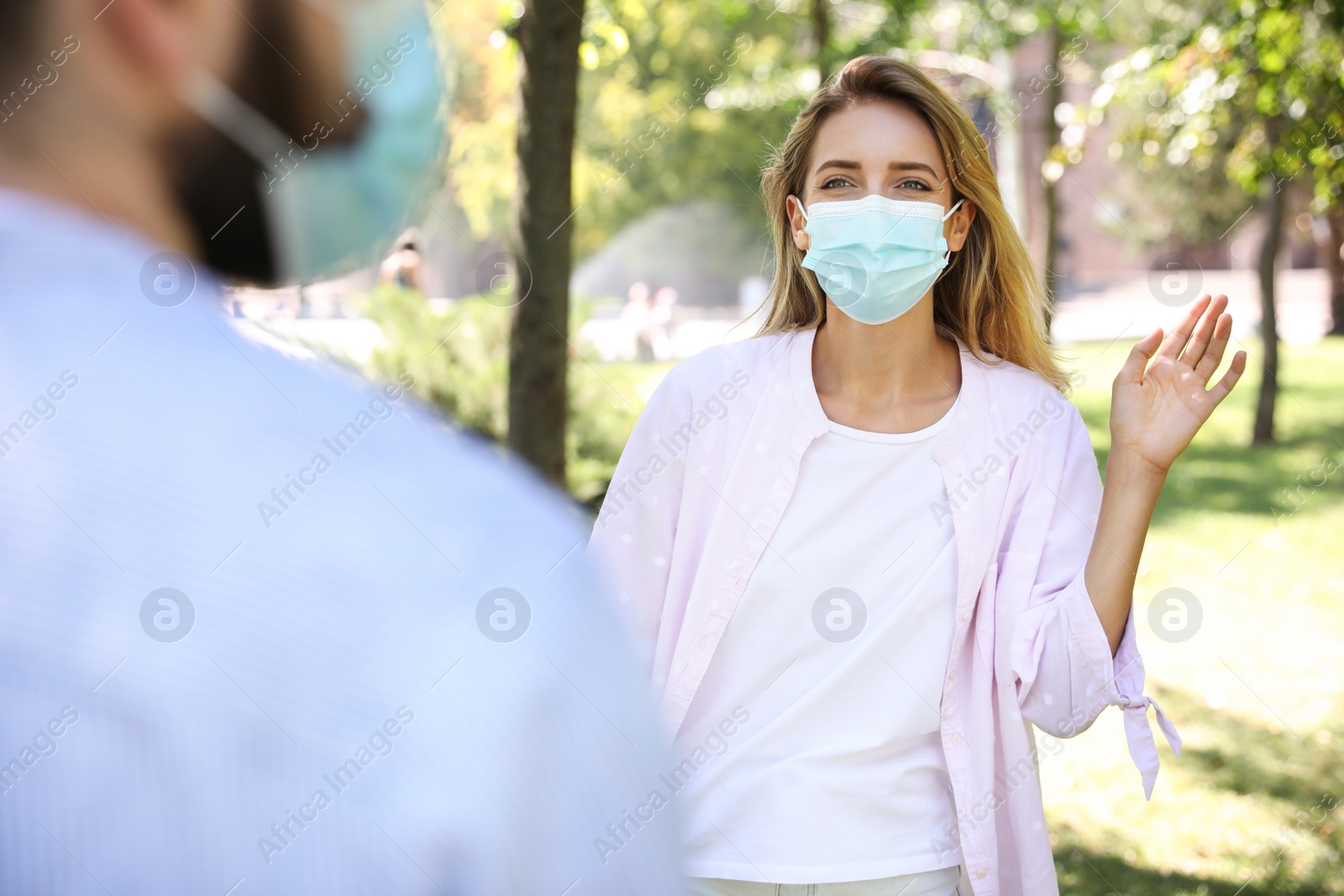 Photo of Woman in protective face mask saying hello outdoors. Keeping social distance during coronavirus pandemic