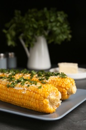 Photo of Delicious boiled corn cobs with butter and parsley on gray table