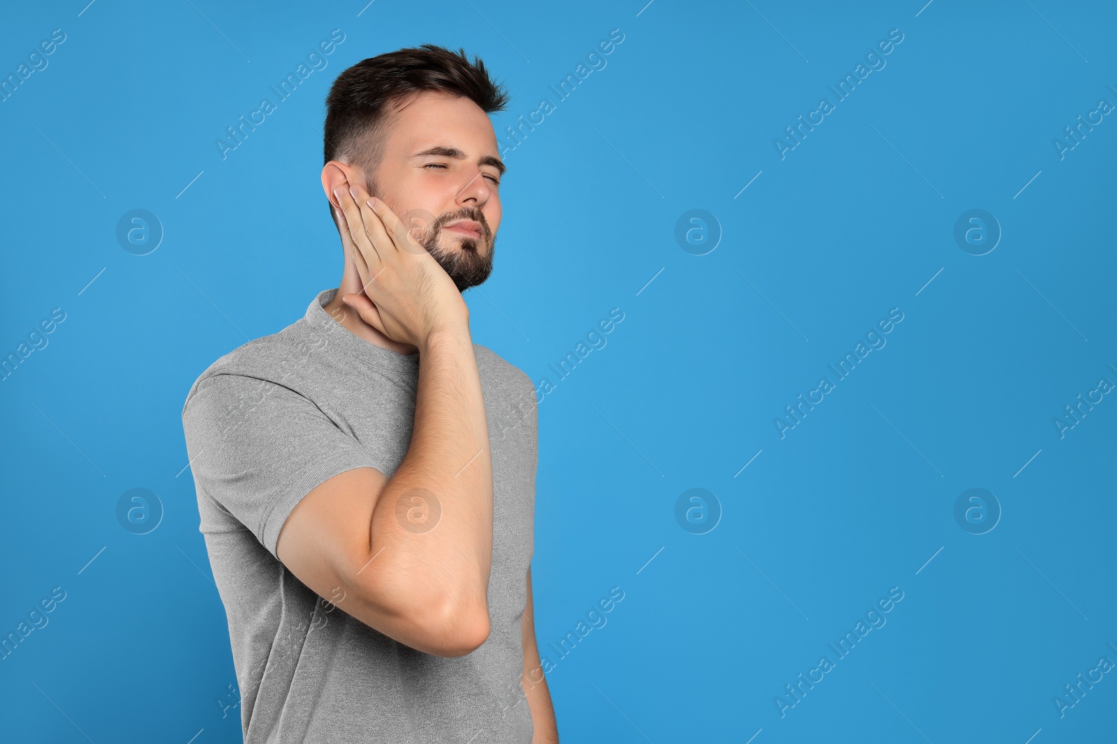 Photo of Young man suffering from ear pain on light blue background. Space for text