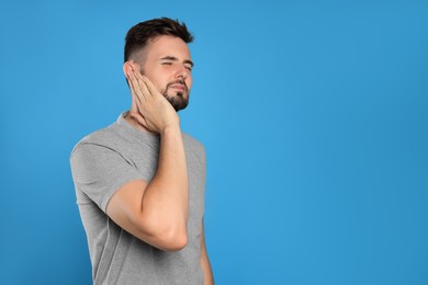 Young man suffering from ear pain on light blue background. Space for text