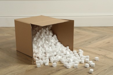 Photo of Overturned cardboard box with styrofoam cubes on wooden floor indoors