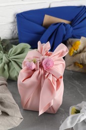 Photo of Furoshiki technique. Many gifts packed in fabric on grey table