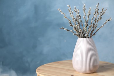 Beautiful bouquet of pussy willow branches in vase on wooden table. Space for text