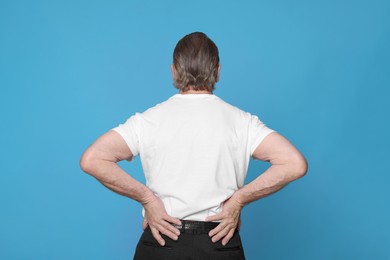 Photo of Senior man suffering from pain in back on light blue background. Arthritis symptoms