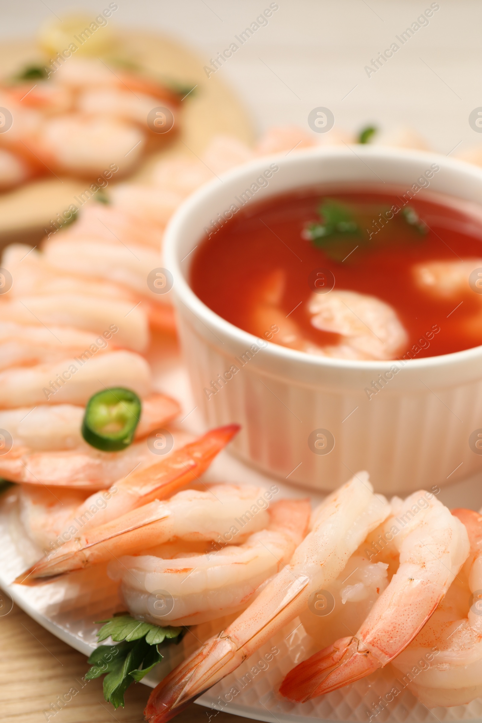 Photo of Tasty boiled shrimps with cocktail sauce, chili and parsley on light wooden table, closeup