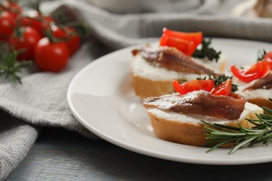 Delicious sandwiches with cream cheese, anchovies and tomatoes on grey wooden table, closeup. Space for text