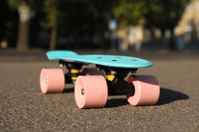 Photo of Light blue skateboard with pink wheels on asphalt outdoors