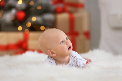 Cute little baby on faux fur against blurred Christmas tree and gift boxes