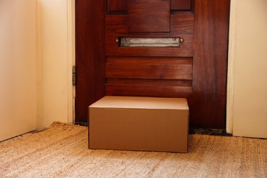 Photo of Delivery service. Cardboard on rug near wooden door indoors